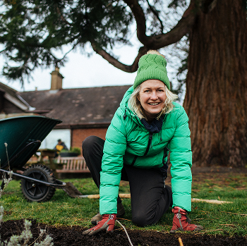 A woman with a smile on her face gardening, leaning down to the ground