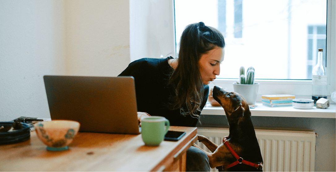 A woman next to a laptop with a dog near the table